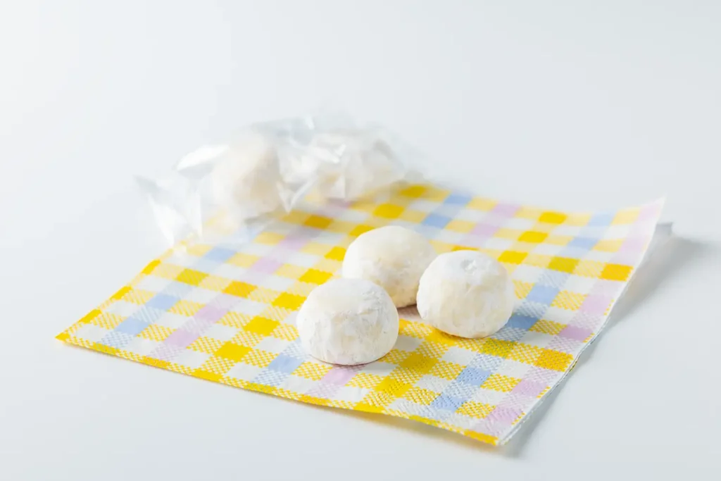 黄色いチェックの紙に置かれた、清雅園の和風クッキー 白くまるい形状で粉がかかっている