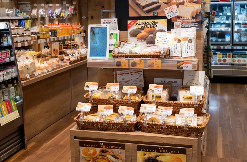 F&F店舗内のグルテンフリー米粉パン売り場。陳列棚にカゴが段積みされ、個包装された食パンや菓子パンが並べられている。