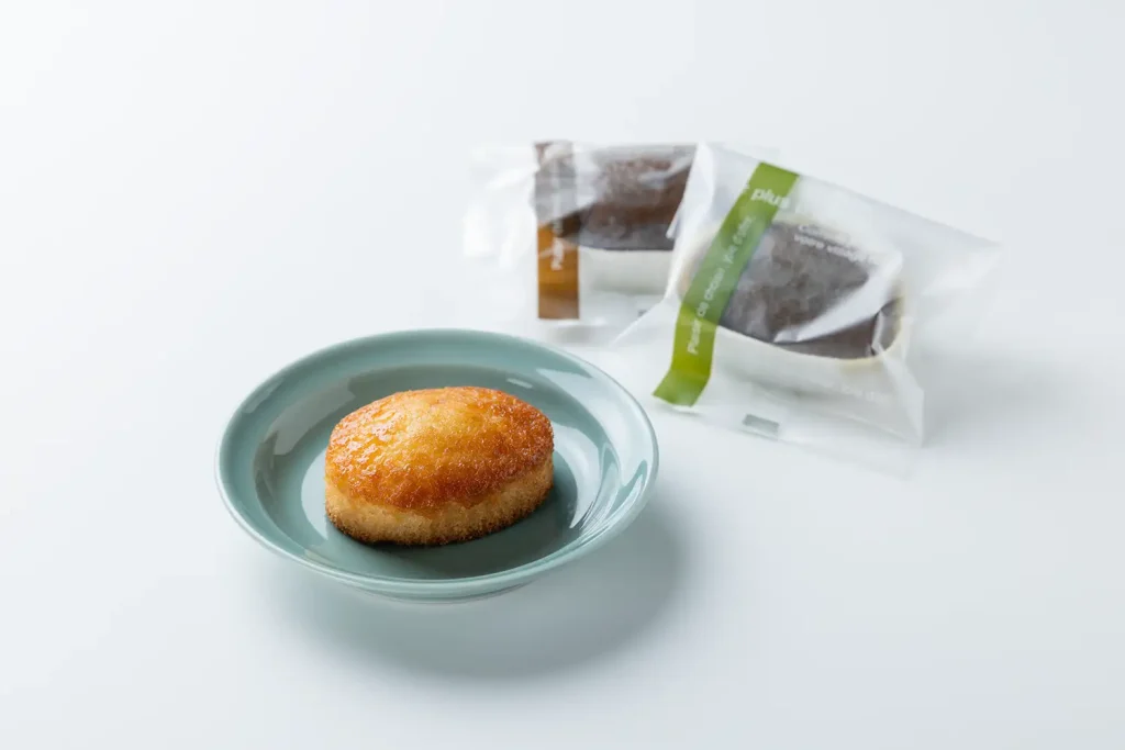 水色の小皿に置かれた丸い米粉のフィナンシェ。表面は焼き色が濃く、横には個包装されたフィナンシェのパッケージが二つ写っている。