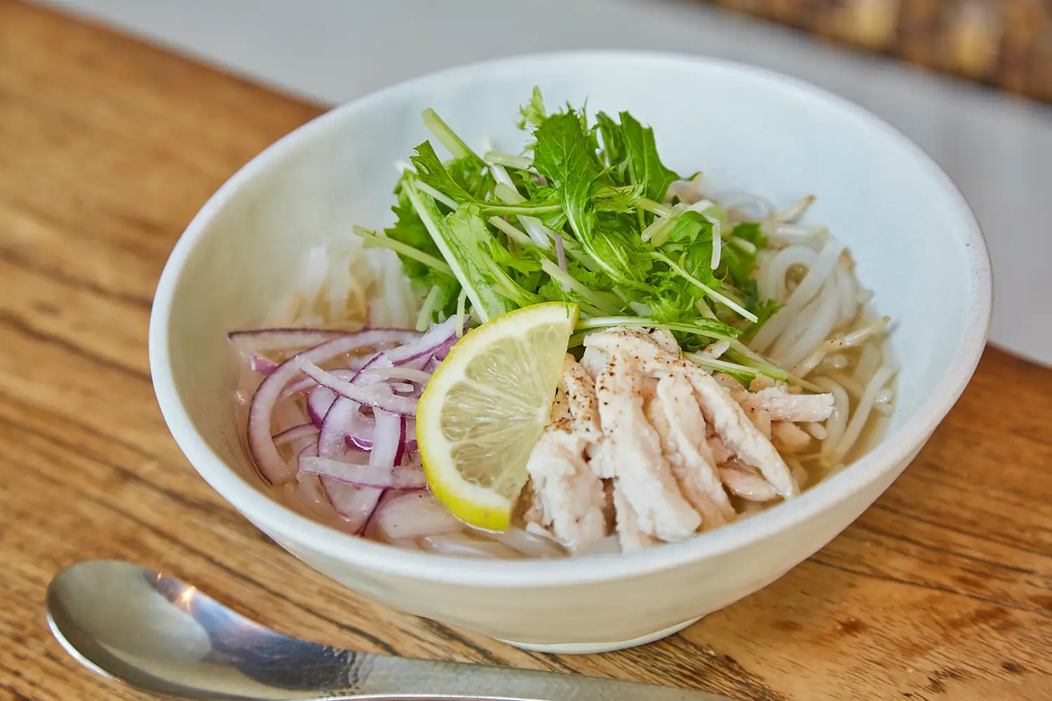 白い器に盛られた国産鶏のフォー。麺のほか香草、レモン、紫玉ねぎ、鶏肉などが盛られている。