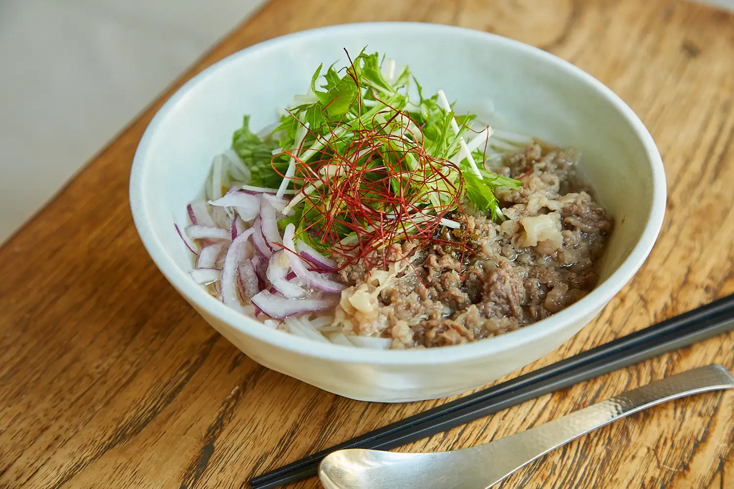 白い器に盛られた神戸牛のフォー。香草、紫玉ねぎ、牛肉などが盛られている。