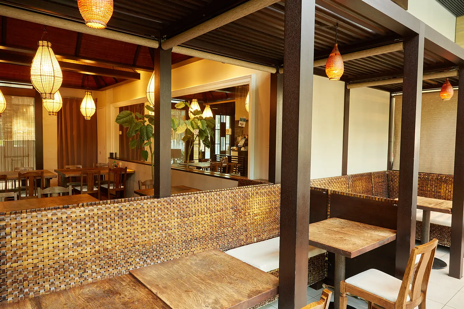 COMPHO with TERRACE 大崎シンクパーク店の店内。編み込み素材のベンチソファと木製のテーブルが並び、アジアンテイストな吊り下げ照明が見える。