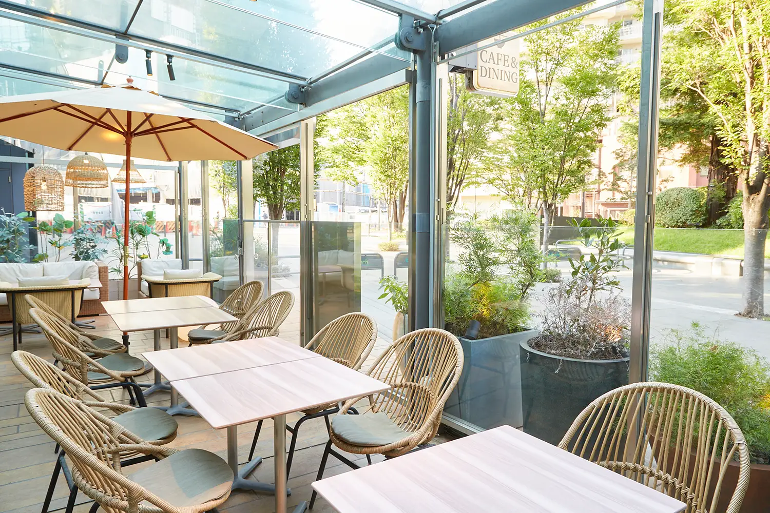 COMPHO with TERRACE 大崎シンクパーク店のガラス張りのテラス席。パラソルと椅子、ソファー席があり、テラスの外には多くの緑が見える。